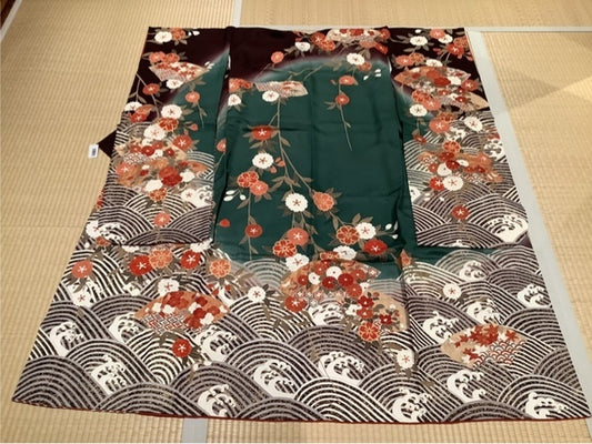 Furisode (long-sleeved kimono) in deep reddish-purple and dark green, featuring double cherry blossoms, peonies, camellias, autumn leaves, chrysanthemums, and a blue wave pattern [4570191658176]